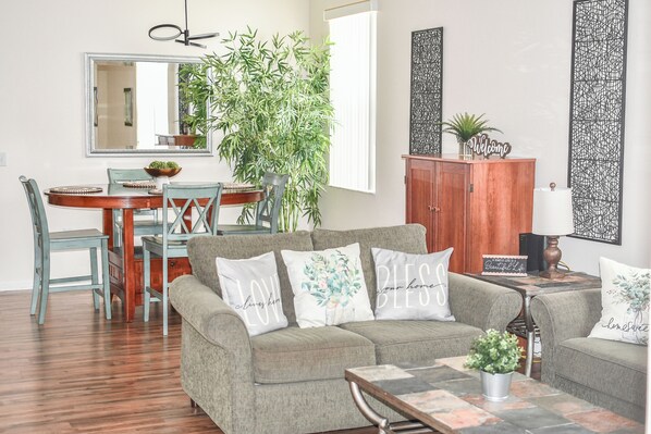 A living room with a sofa, a coffee table, a dining table with chairs, a large plant, and a cabinet.