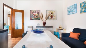 Uma sala de jantar com uma mesa comprida, cadeiras, um vaso e duas pinturas na parede.