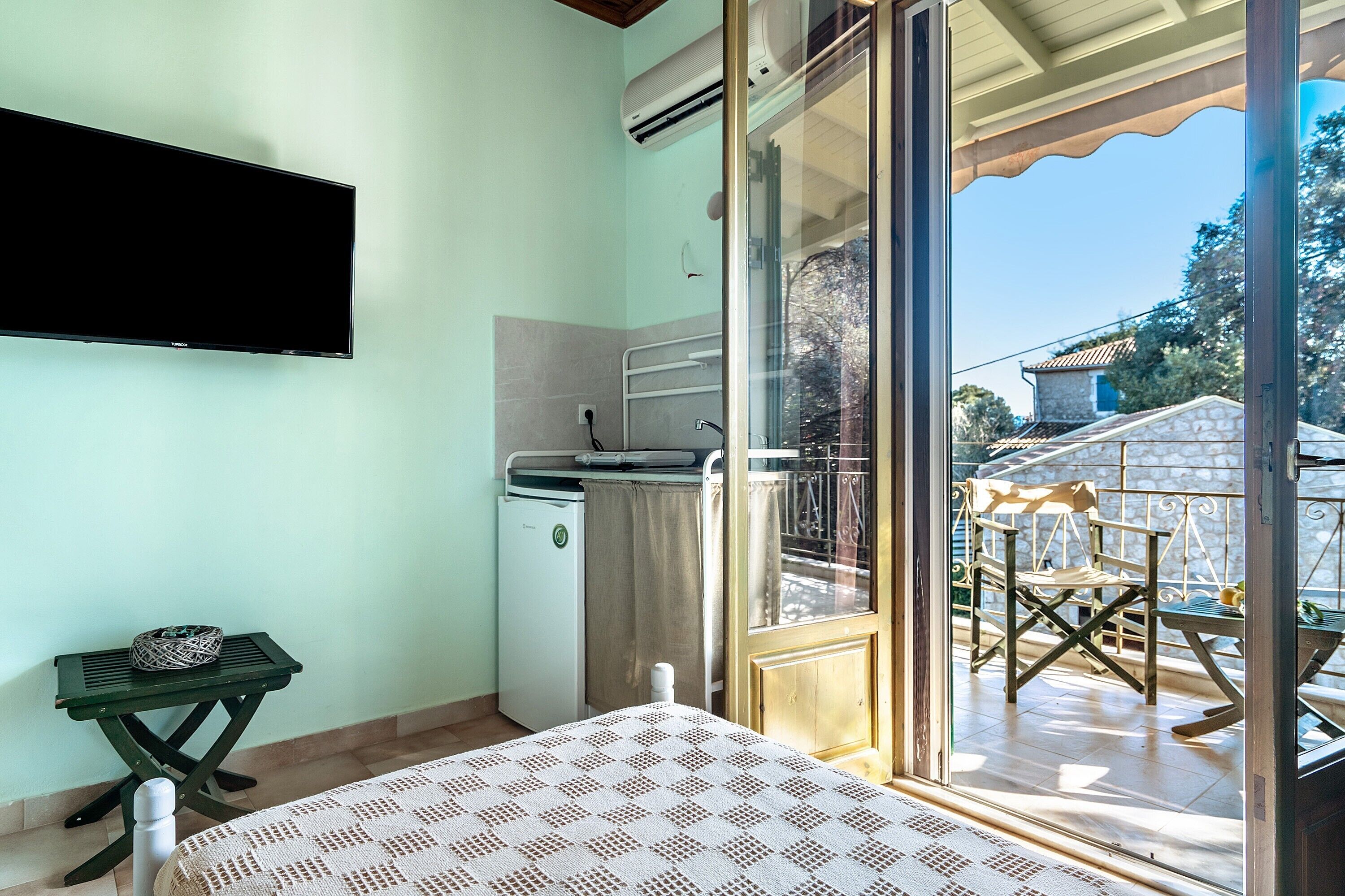 Una habitación con cama, una mesita con un bolso, lavadora y una puerta corrediza de vidrio que da a un espacio exterior con una mesa y sillas.