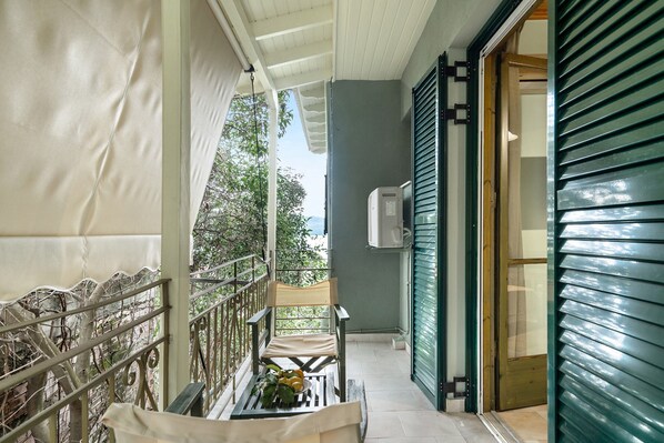 A covered balcony with a chair, a table with lemons, and a view of greenery.