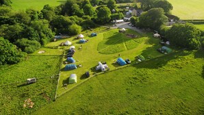 An aerial view of a campsite with tents and caravans arranged in a circular pattern, surrounded by lush green fields and trees. - Hideaway Escapes (Narberth)