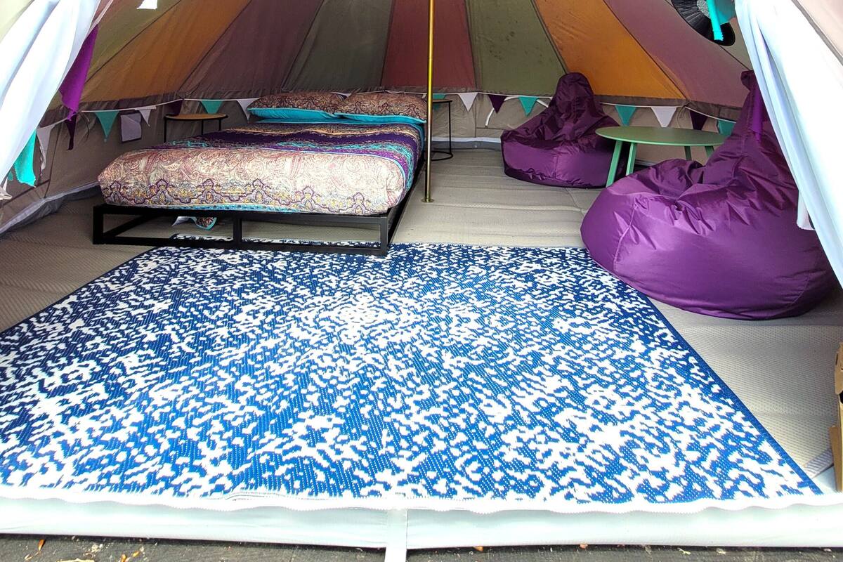 Een tent met een bed, een blauw patroonmatje en paarse schapenvachtjes.