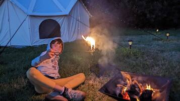 A person sitting by a campfire with a tent and a portable stove in the background.