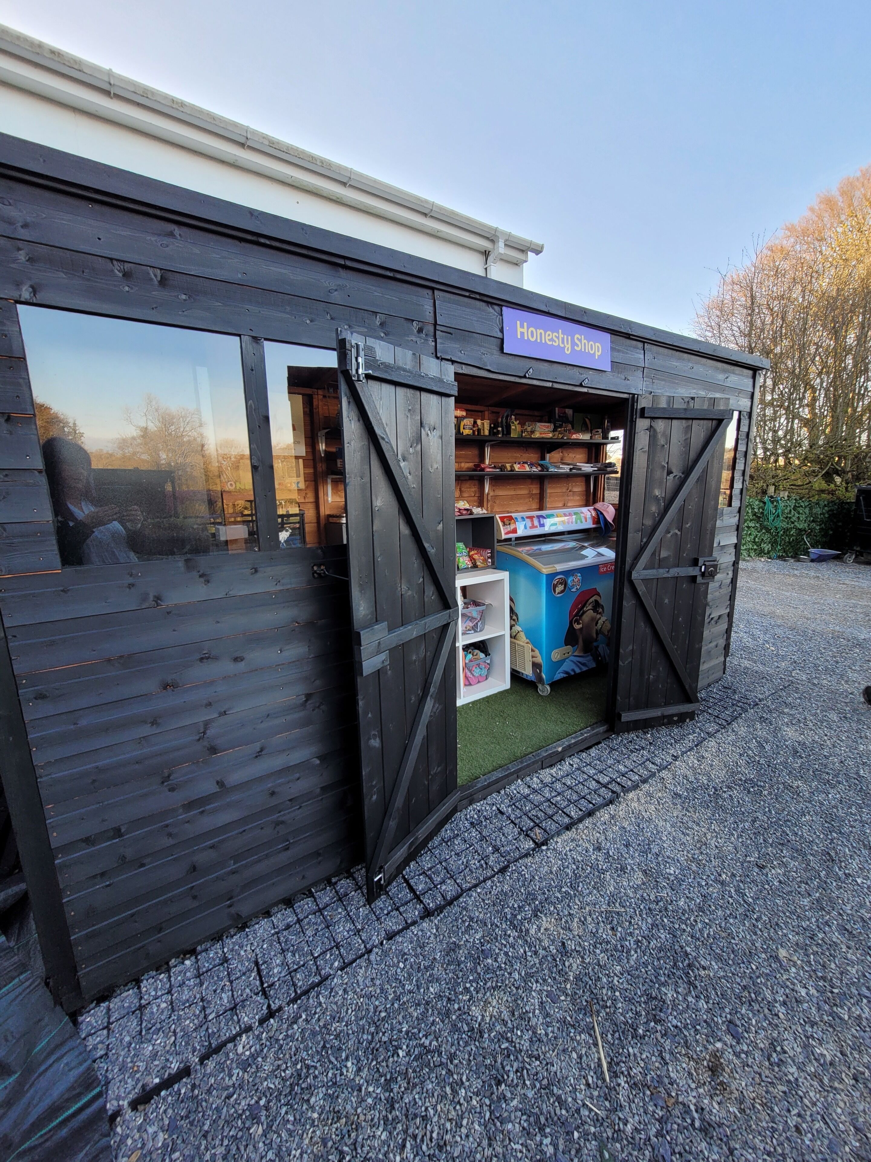 A wooden shop with a sign reading "Honesty Shop" and a display of ice cream.