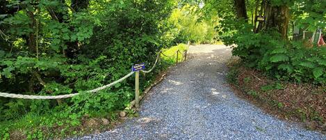 A gravel pathway leading through a wooded area with a rope barrier and a sign indicating a parking area.