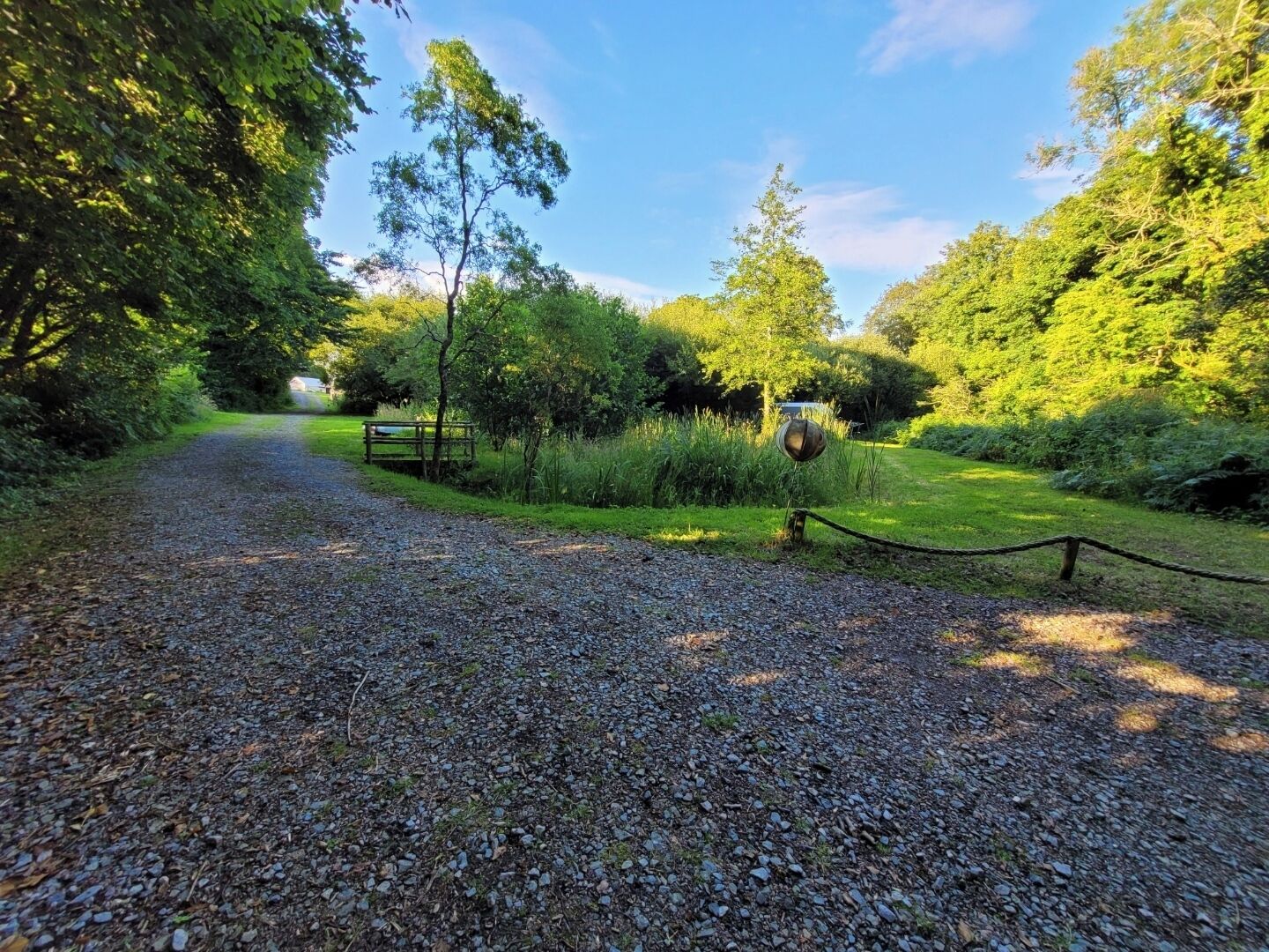 A gravel path leading through a park with trees and a metal sculpture.