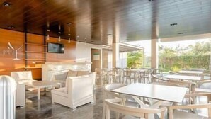 Un ristorante moderno con arredi bianchi, soffitto in legno e ampie finestre che si affacciano sul verde.