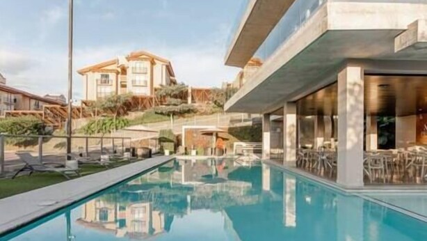 Un'area piscina moderna con acqua cristallina, lettini prendisole e un edificio con ampie vetrate sullo sfondo.