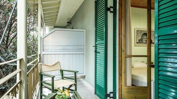 Ein Balkon mit Stuhl und Tisch, eine grüne Tür und eine weiße Wand mit einem Fenster.