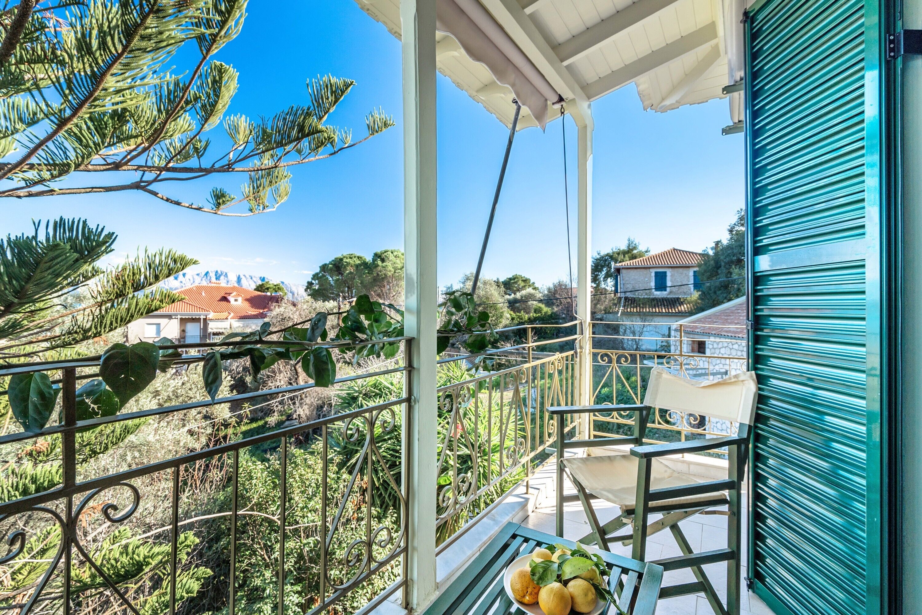 A balcony with a view of a mountainous landscape, a table with fruits, and a blue door.