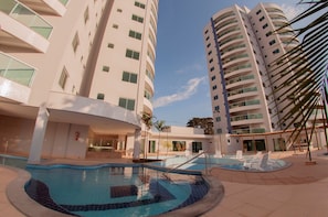 Un hotel moderno con area piscina, diversi balconi e cielo sereno.