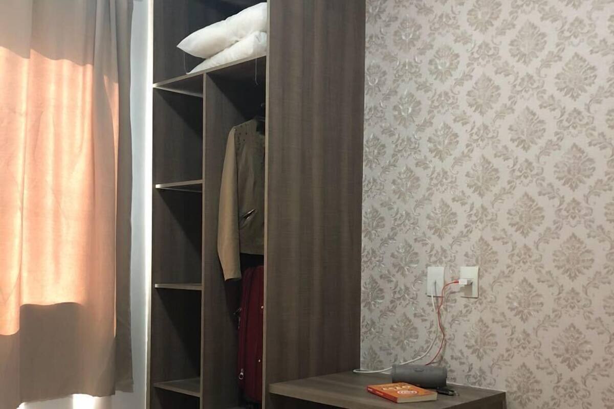 A bedroom with a bed, a wardrobe, a desk, and a patterned wallpaper.