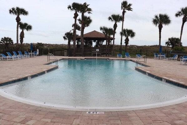 A swimming pool with a gazebo, palm trees, and lounge chairs.