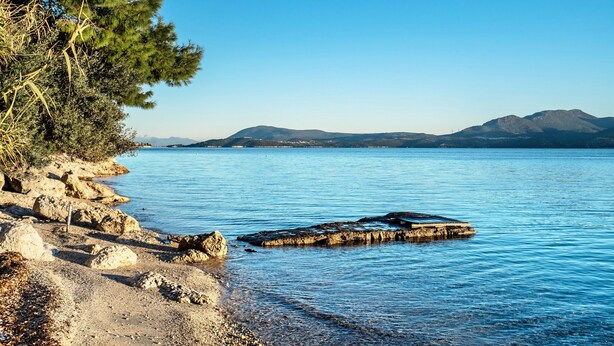 Un paysage côtier caractérisé par une rive rocheuse, une eau calme et des montagnes lointaines.