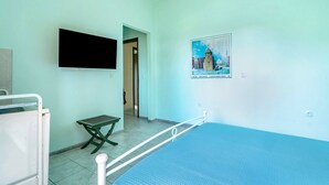 Un dormitorio con una cama, un televisor montado en la pared, una mesita pequeña y un cartel.