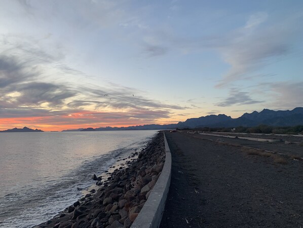 A coastal road with a rocky shoreline and mountains in the background.