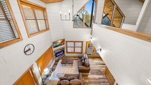 Intérieur d’une cabane en bois à plusieurs niveaux, doté d’une cheminée, d’un coin salon et de grandes fenêtres.