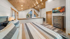 Une chambre avec un grand lit, un plafond en bois et un tableau représentant une cascade.