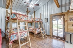 Des lits superposés avec des couvertures aux couleurs vives, un ventilateur de plafond et une porte en bois donnant sur l’extérieur.