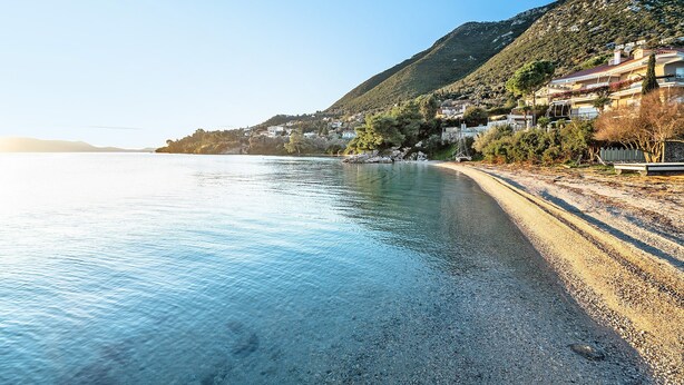 A coastal road with a pebble beach, houses on a hillside, and a clear sky. - Studio Apartment 'Old Boat Double Studio 2' with Sea View, Wi-Fi and Air Conditioning (Lefkada)