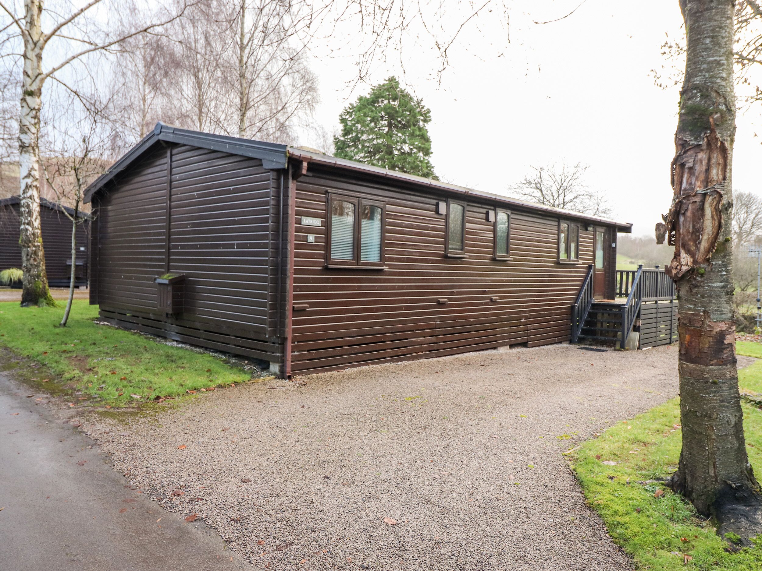 A wooden cabin with a gravel driveway and a wooden deck.