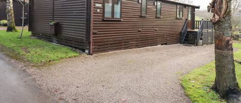 A wooden cabin with a gravel driveway and a wooden deck.