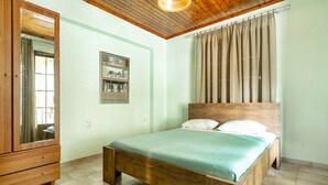 A bedroom with a wooden bed, a wardrobe, a framed picture on the wall, and a window with curtains. - Apartment 'Old Boat' with Sea View, Wi-Fi and Air Conditioning (Lefkada)