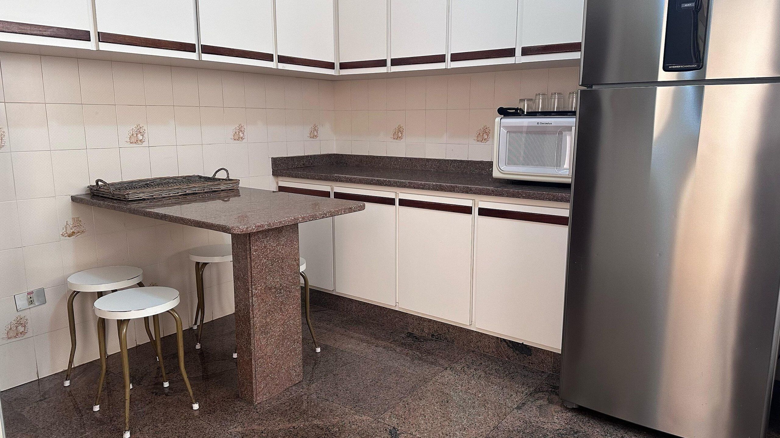 A kitchen with a granite countertop, white cabinets, a stainless steel refrigerator, and two bar stools.