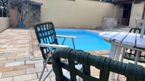 A poolside area with a pool, a chair, and a table. - Recanto Amana Casa Centro de SJBVista (Sao Joao da Boa Vista)