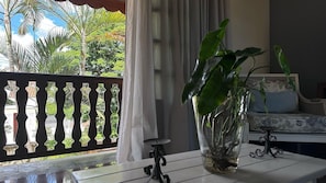 A room with a table, a potted plant, a sofa, and a balcony with a railing.