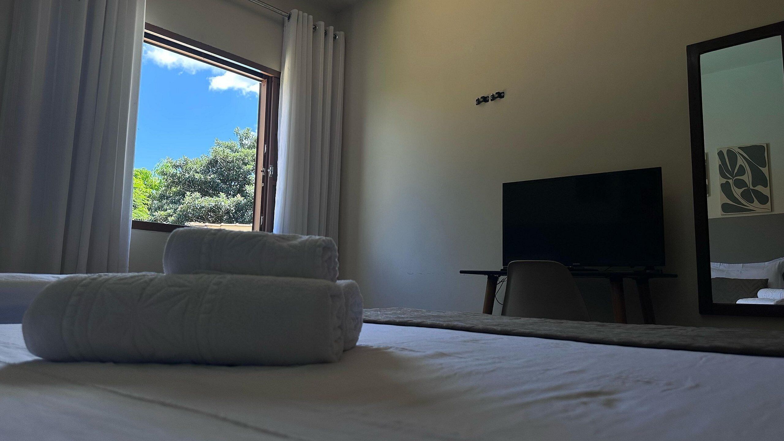 Een hotelkamer met een bed, een televisie, een raam met gordijnen en uitzicht op groen.