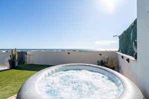 Un toit-terrasse avec un jacuzzi, un cactus et une vue sur la mer.