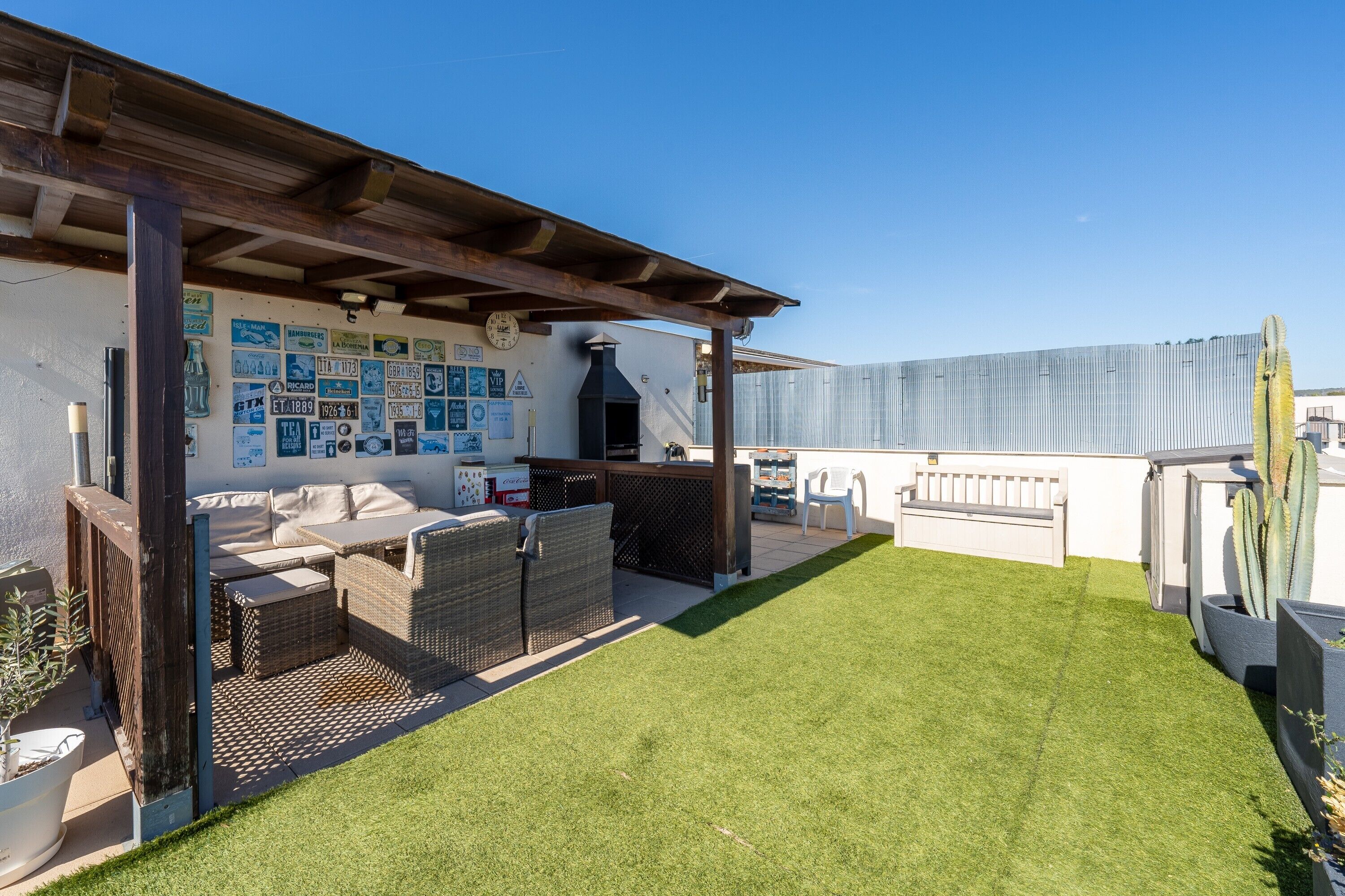 A rooftop patio with outdoor furniture, a grill, and a wall decorated with various signs.