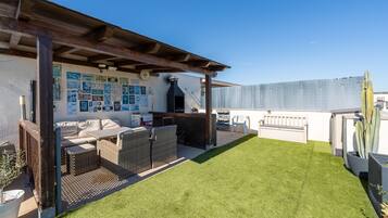 A rooftop patio with outdoor furniture, a grill, and a wall decorated with various signs.