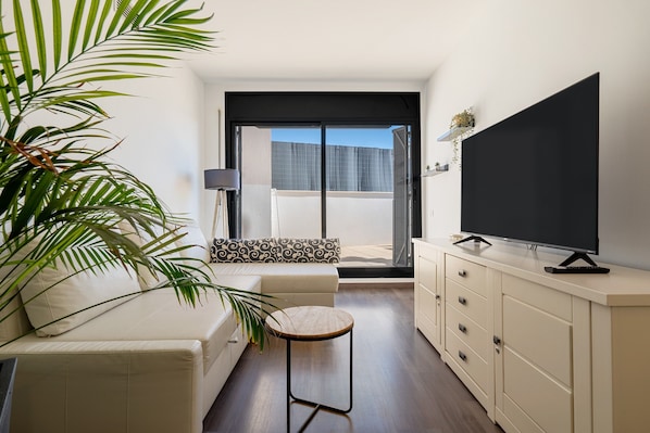 Un salon moderne avec un canapé, une petite table ronde, un téléviseur posé sur un meuble et une porte-fenêtre coulissante donnant sur un balcon.