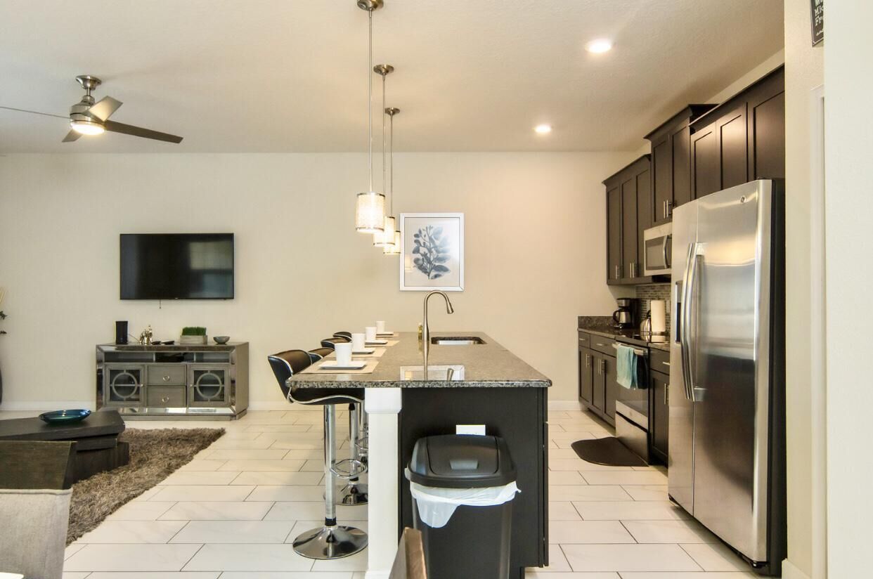 A modern kitchen with a central island, stainless steel appliances, and a flat-screen TV mounted on the wall.