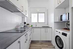 Una cocina moderna con armarios blancos, lavadora integrada y una ventana sobre el fregadero.