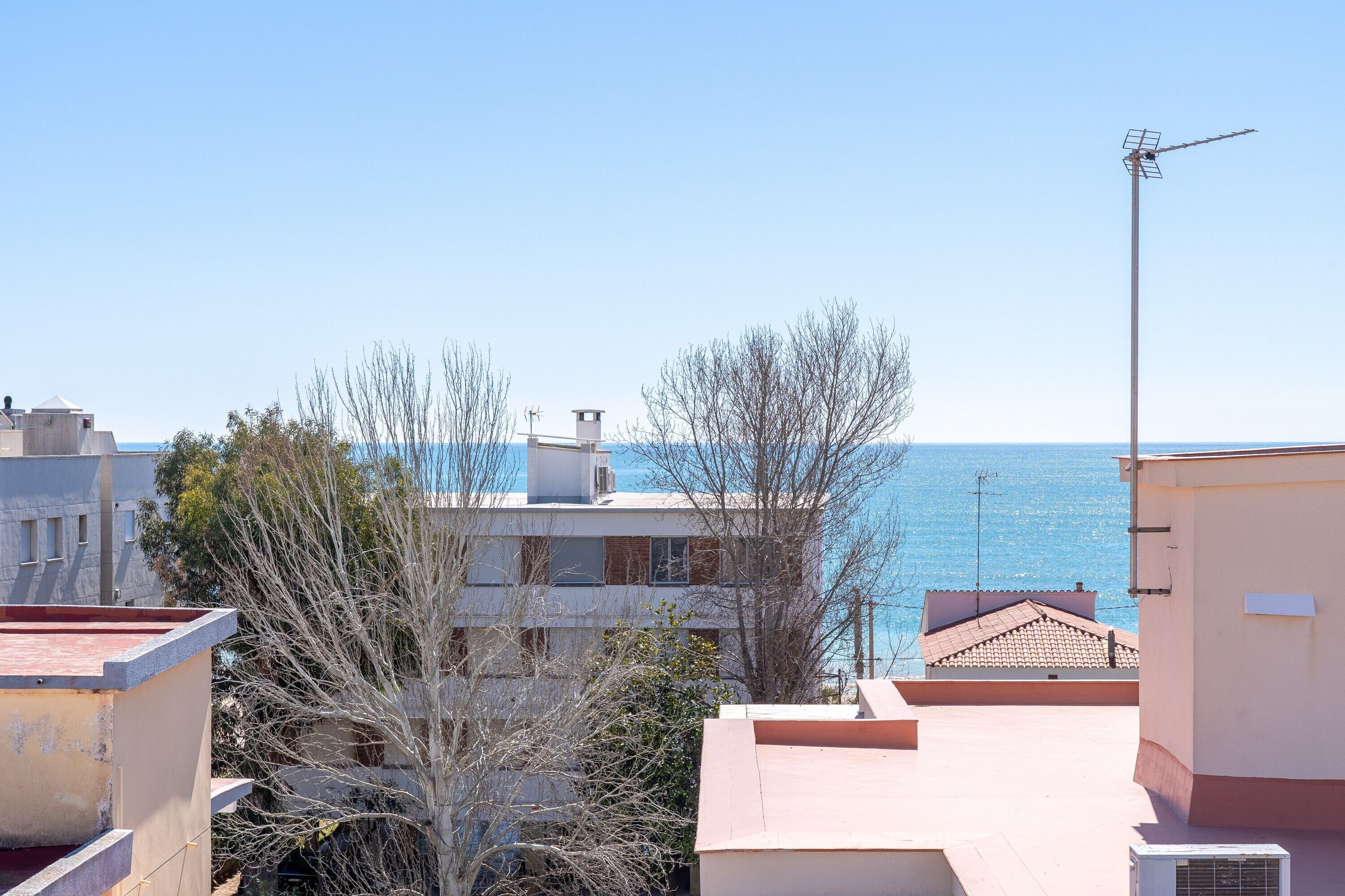 A coastal residential area with buildings, a clear sky, and the sea in the background.