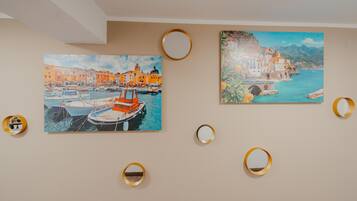 Two paintings of coastal scenes with boats, framed by gold rings on a plain wall.