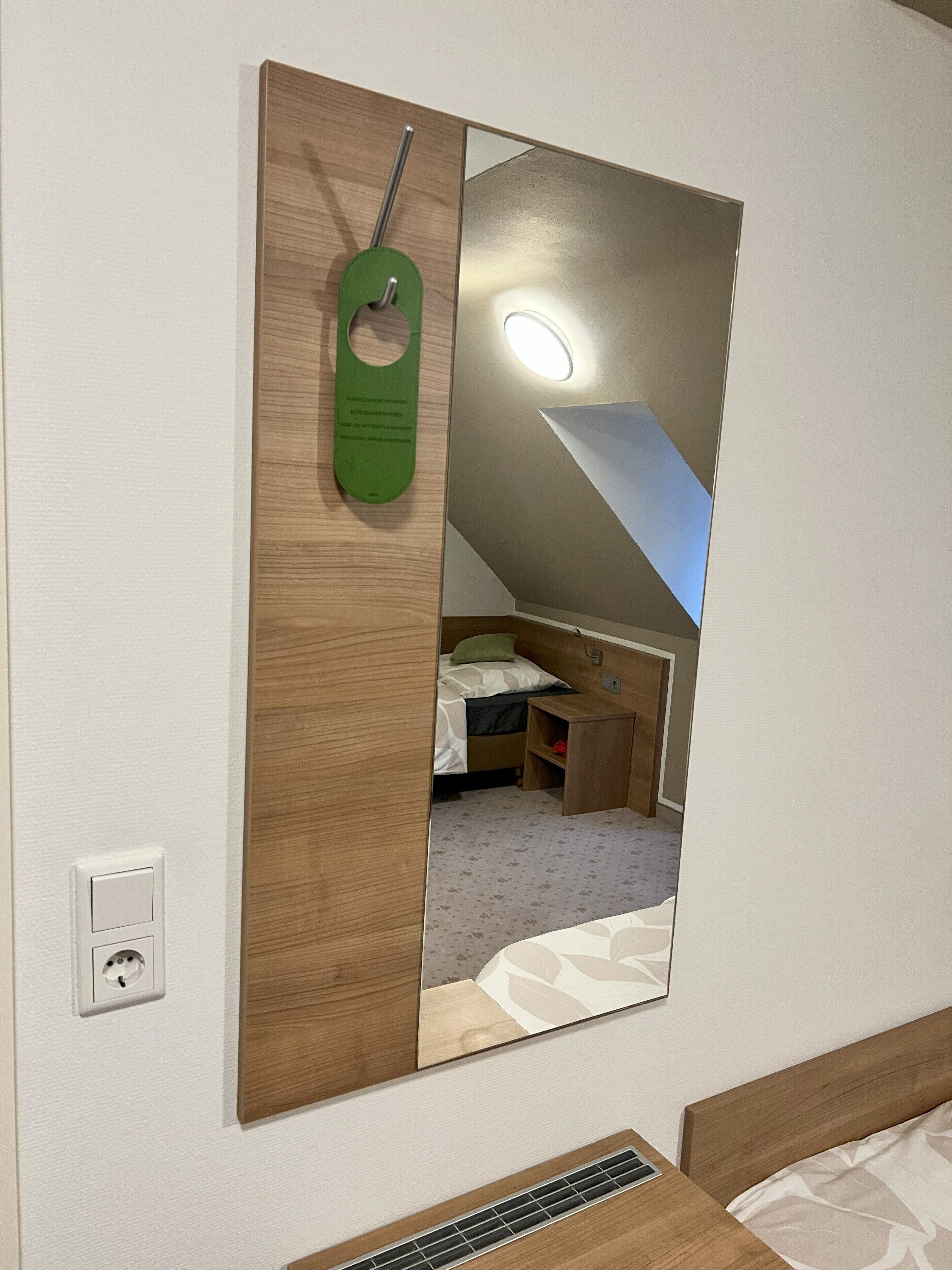 Een kamer met een bed, nachtkastje, spiegel en een stopcontact.