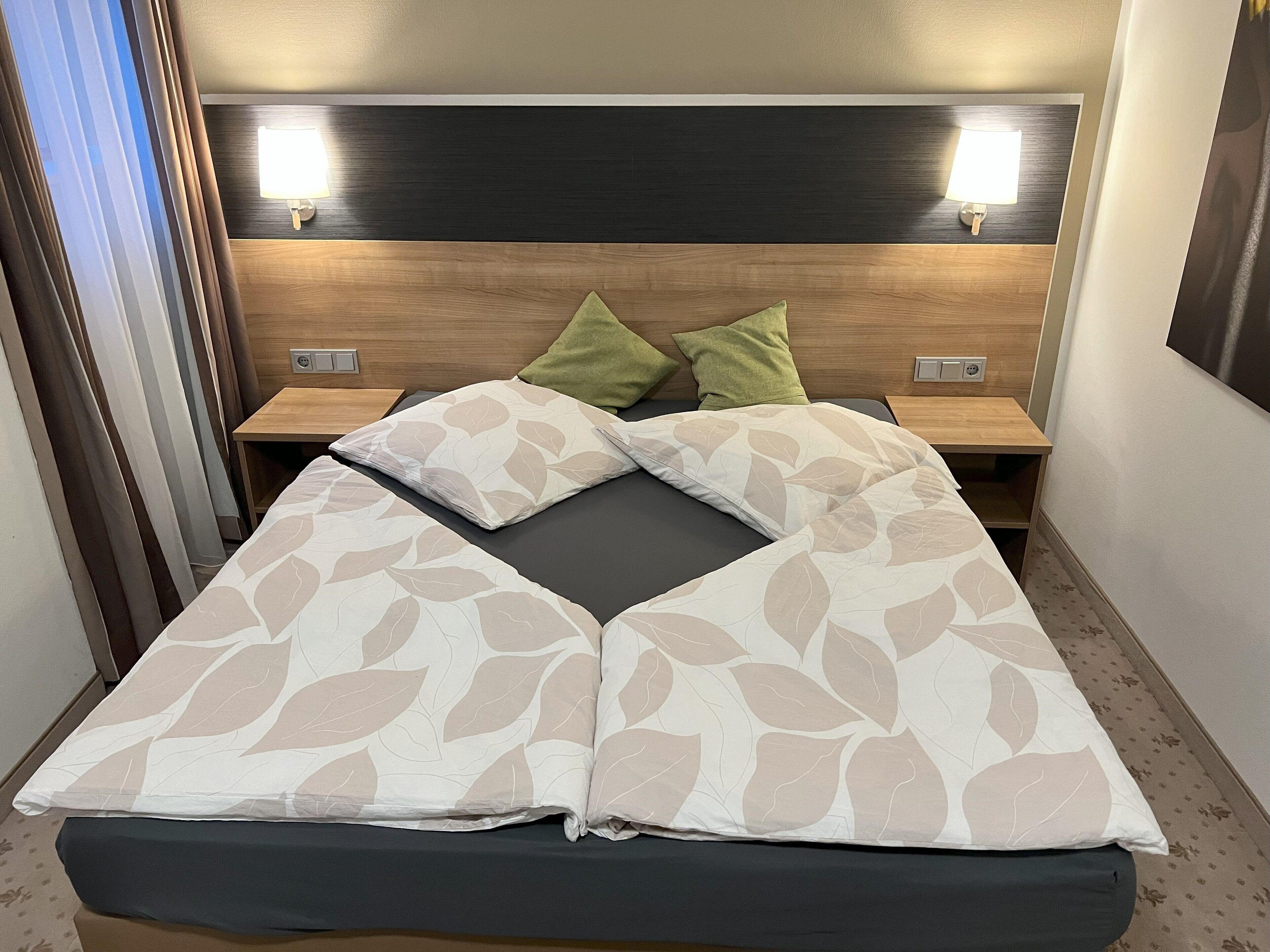 Una cama bien hecha con una colcha de diseño floral, dos lámparas de noche y un cabecero de madera.