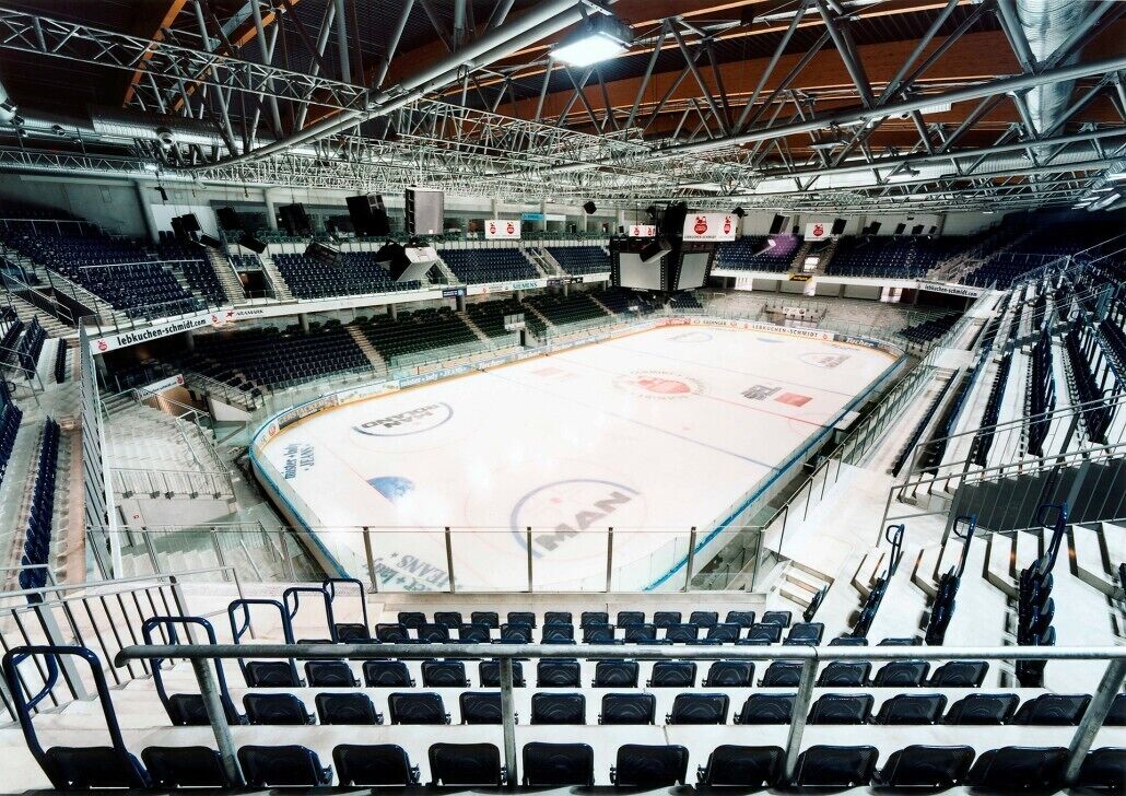 En indendørs ishockeybane med flere sæder og et højt loft med metalbjælker.