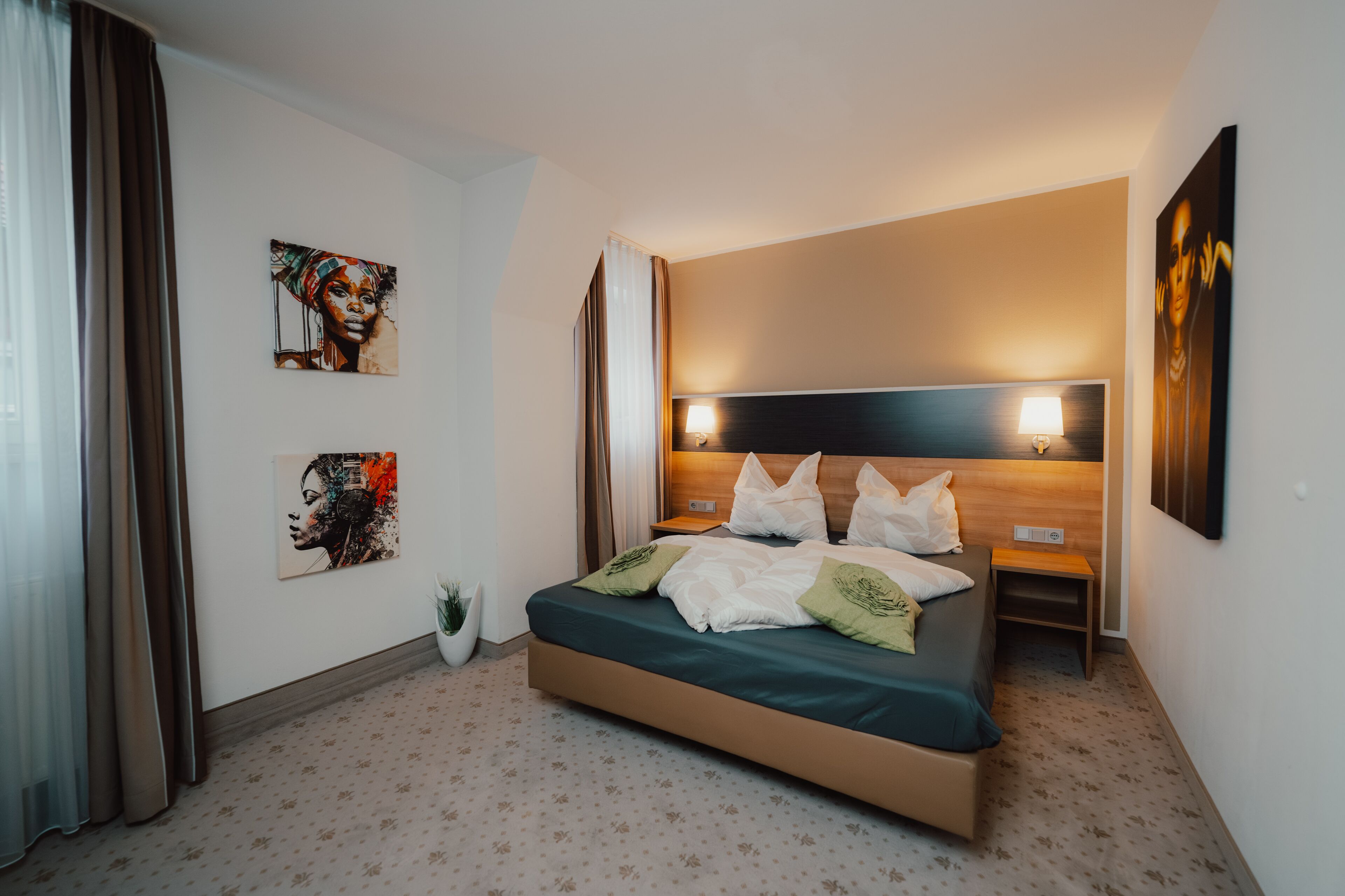 Una habitació d'hotel moderna amb un llit, una taula de nit, una làmpada de paret i dues obres d'art.