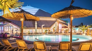 Un espace piscine doté de chaises longues et de parasols, entouré d’un bâtiment au design moderne.