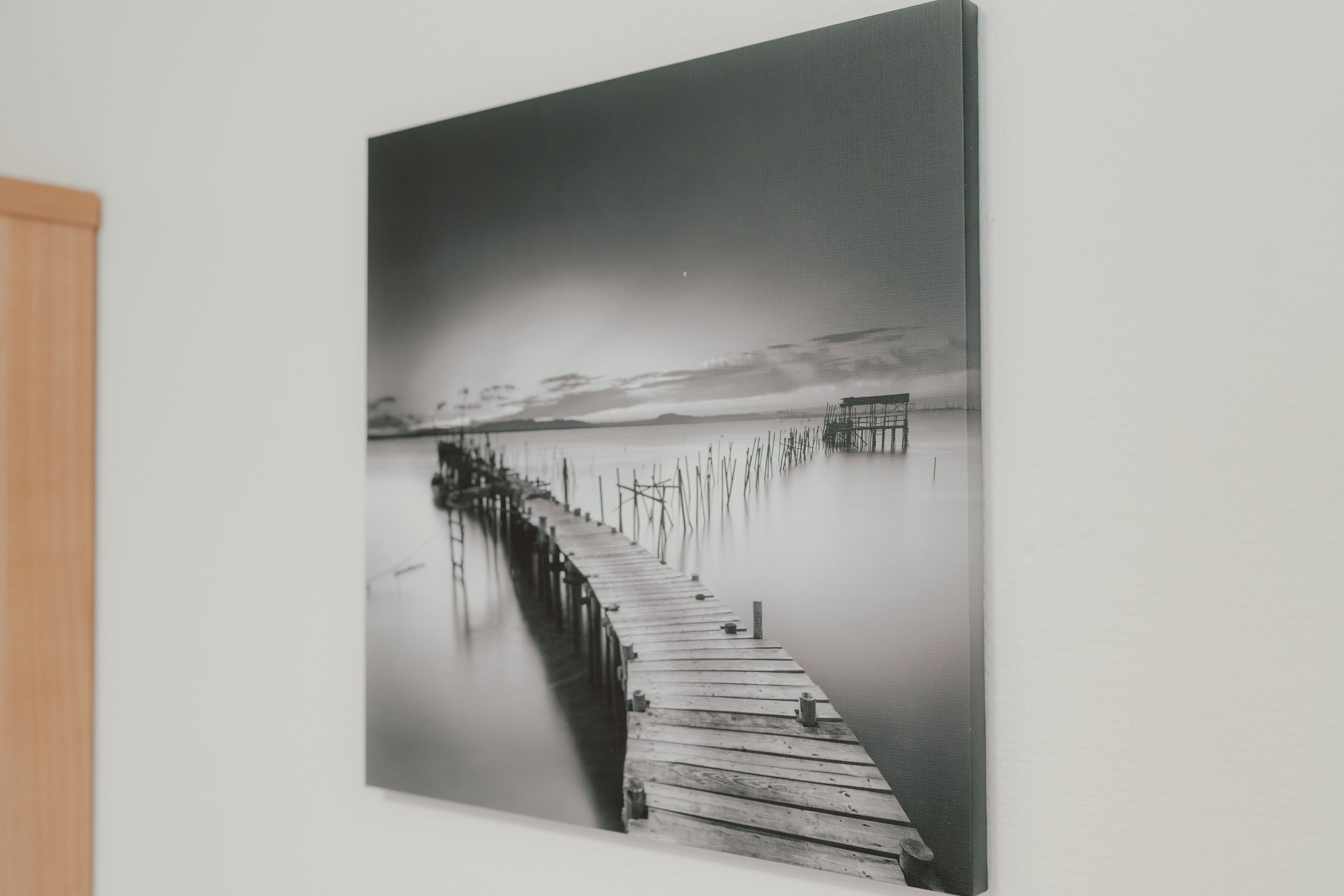 A black and white photograph of a wooden pier extending into calm water, with a structure at the end.