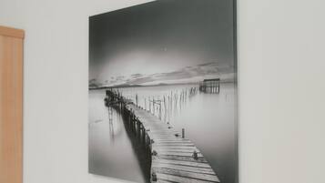 A black and white photograph of a wooden pier extending into calm water, with a structure at the end.