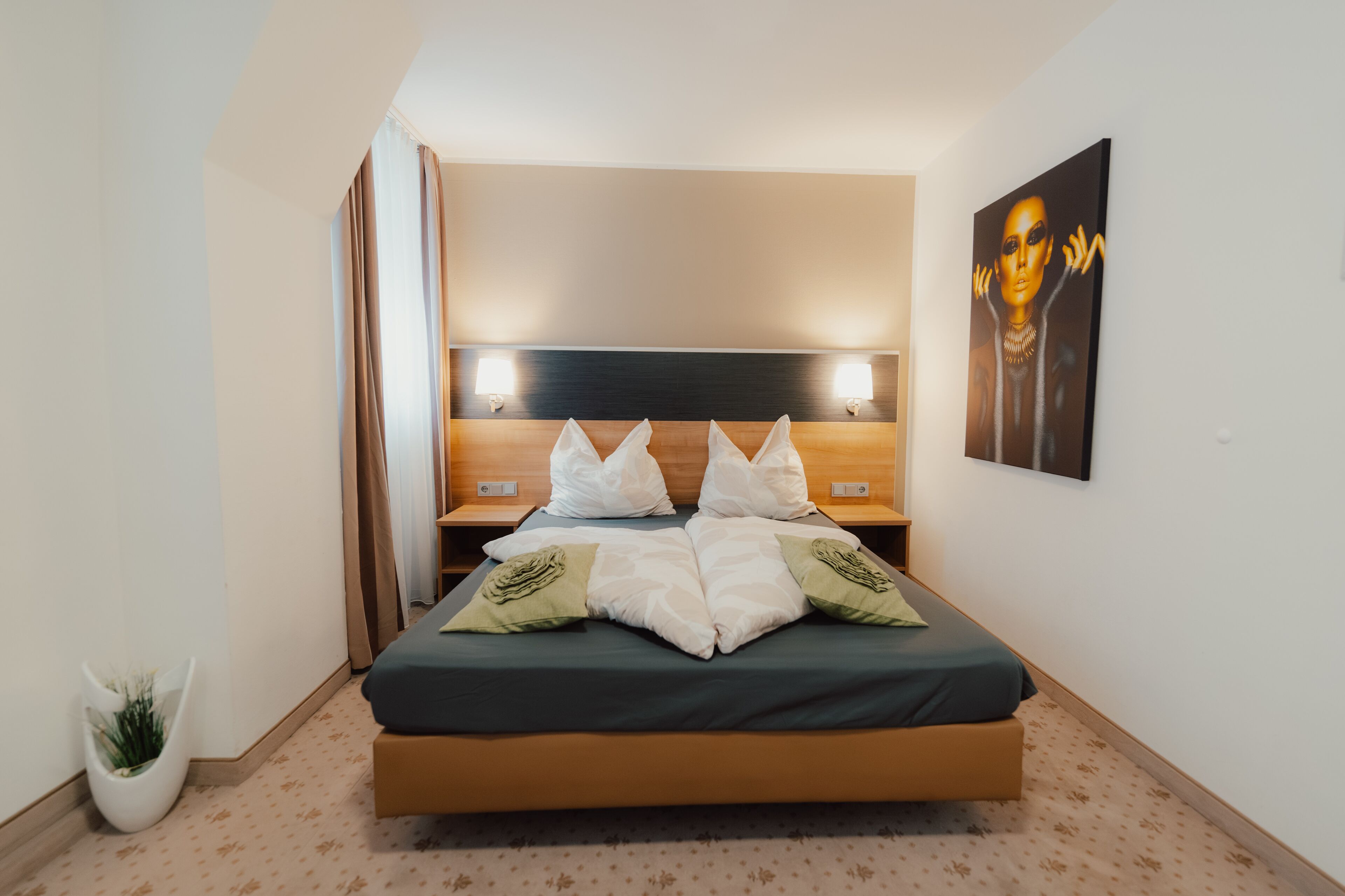 Una habitación de hotel moderna con una cama grande, mesitas de noche, un cuadro colgado en la pared y una planta en maceta.