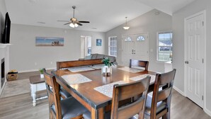 A dining area with a wooden table, chairs, and a ceiling fan. There are two doors and windows in the background. - Homey 3/2, near Fleming Island (Middleburg)