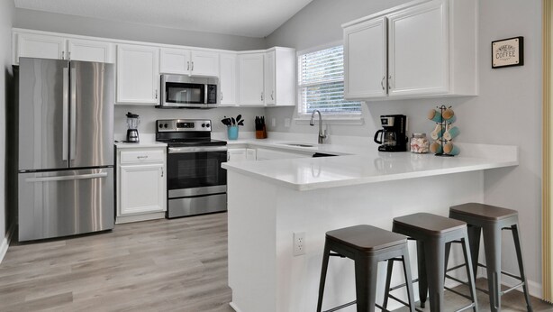 A modern kitchen with white cabinetry, stainless steel appliances, a central island with stools, and a coffee machine. - Homey 3/2, near Fleming Island (Middleburg)