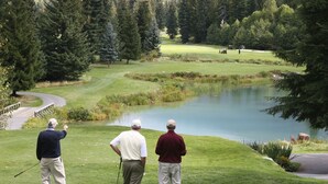 Un campo de golf con un estanque, rodeado de árboles.